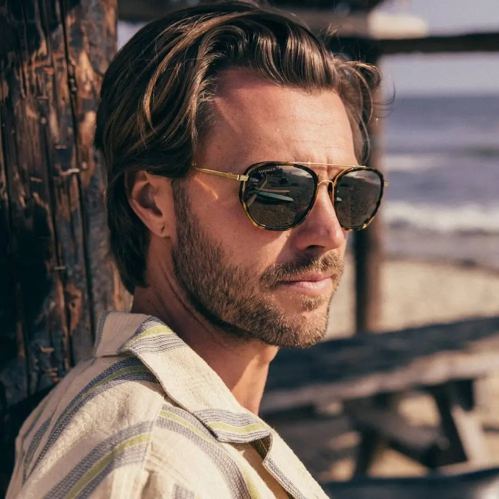 man met halflang haar en baard draagt zonnebril op strand