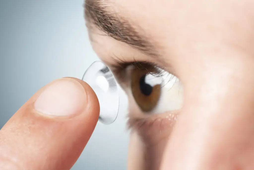Vinger die contactlens richting bruin oog brengt